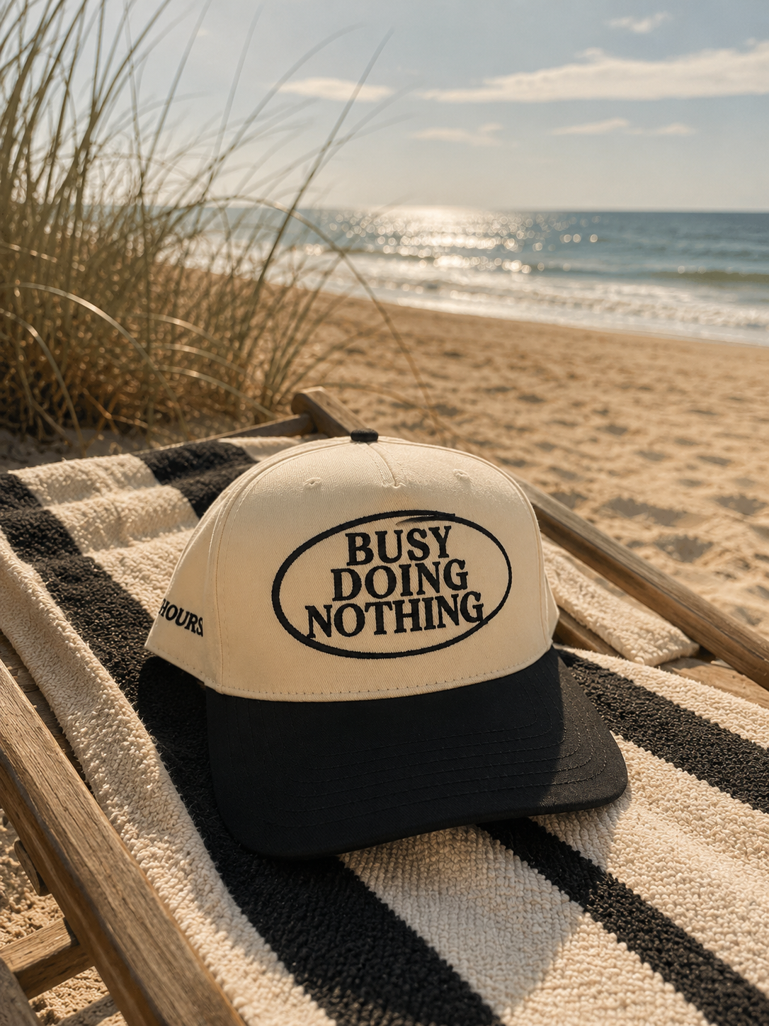 Busy Doing Nothing black and natural trucker hat by Off Hours on a beach chair