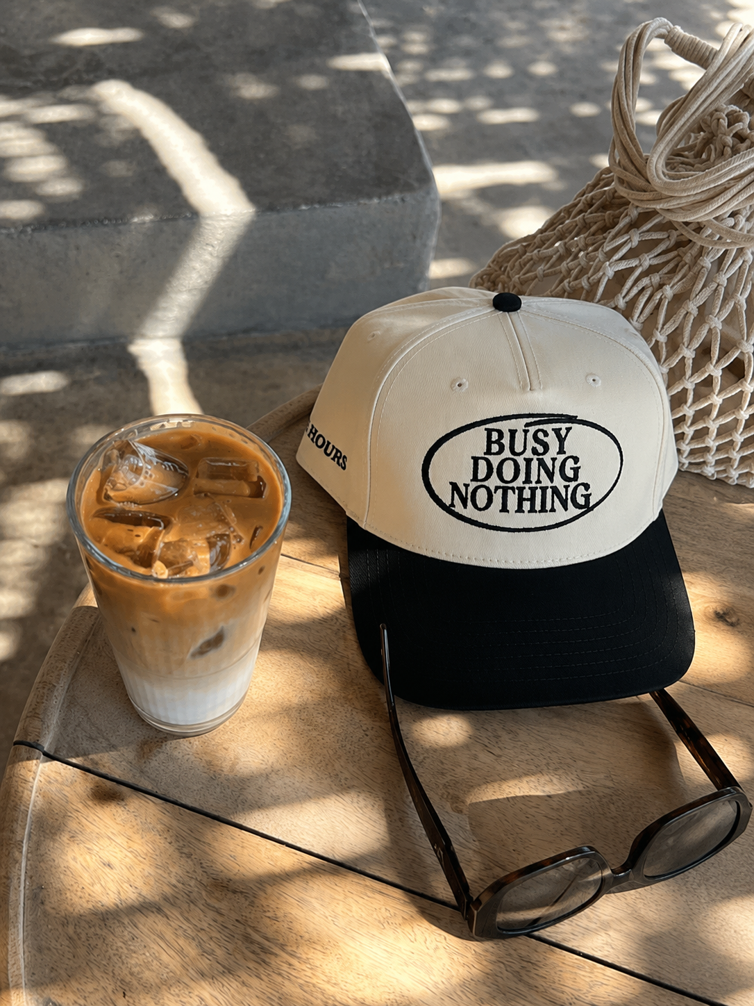 Busy Doing Nothing black and natural trucker hat by Off Hours with coffee and sunglasses